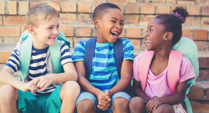 kids sitting outside brick building with backpacks on