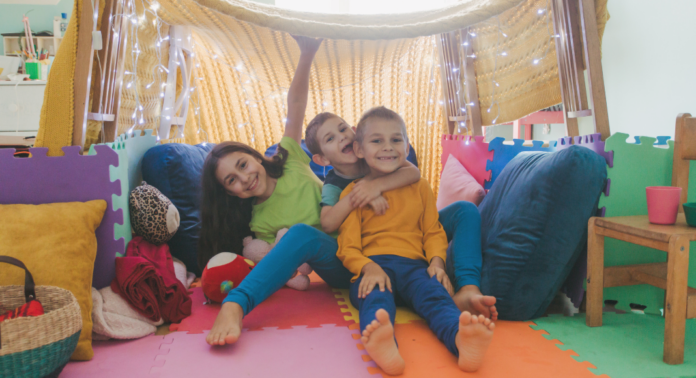 three children smiling while sitting inside of fort